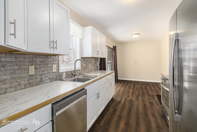 kitchen featuring appliances with stainless steel finishes, a sink, baseboards, decorative backsplash, and white cabinetry