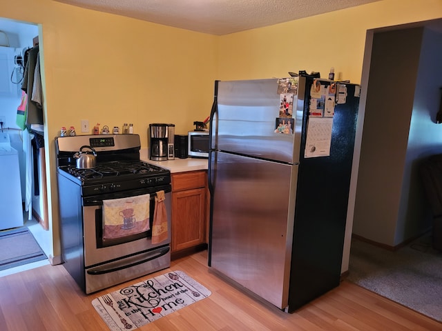 kitchen with a textured ceiling, appliances with stainless steel finishes, washing machine and dryer, and light wood-type flooring