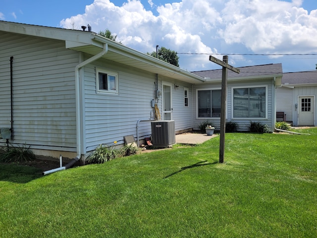 rear view of property featuring a lawn and central air condition unit