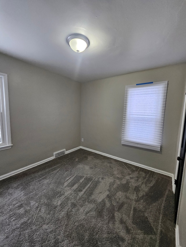 spare room with dark colored carpet and a healthy amount of sunlight