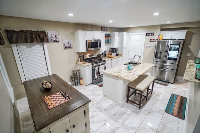 kitchen with sink, stainless steel appliances, white cabinetry, and an island with sink