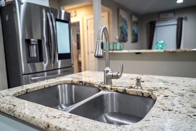 kitchen with sink, stainless steel fridge with ice dispenser, and light stone countertops