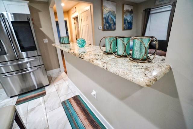 kitchen with light stone counters, light tile patterned flooring, stainless steel fridge, and white cabinetry