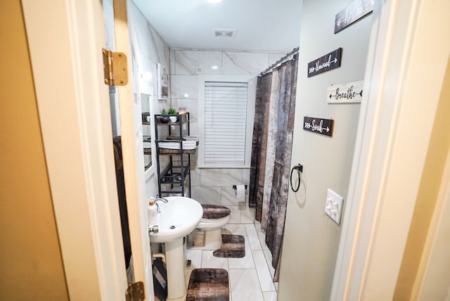 bathroom featuring toilet, tile patterned floors, tile walls, and a shower with curtain