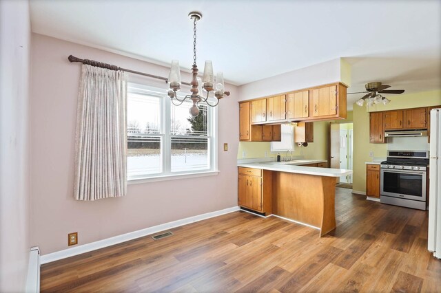 kitchen featuring decorative light fixtures, kitchen peninsula, stainless steel gas range oven, dark hardwood / wood-style floors, and range hood