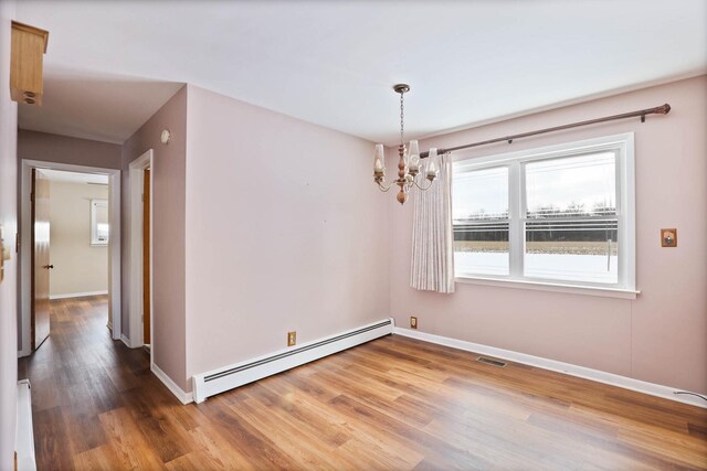 unfurnished room featuring hardwood / wood-style floors, a baseboard heating unit, and an inviting chandelier