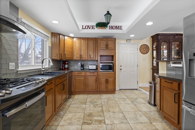 kitchen with sink, stainless steel appliances, wall chimney exhaust hood, tasteful backsplash, and a tray ceiling