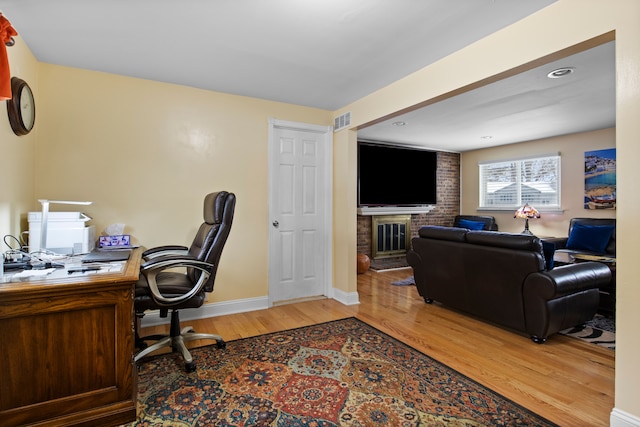 office space featuring wood-type flooring and a brick fireplace