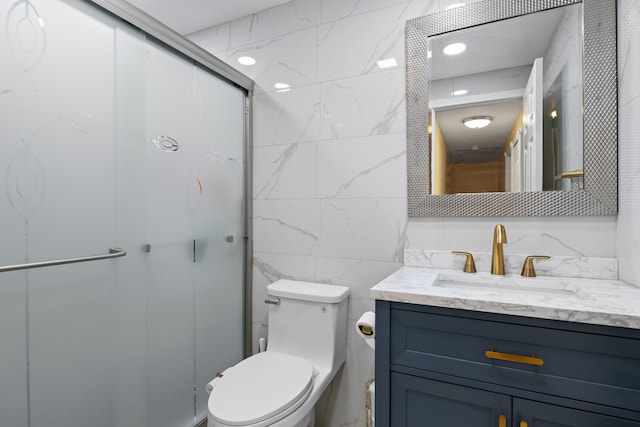 bathroom with tile walls, toilet, vanity, and a shower with shower door