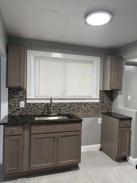 kitchen featuring sink, dark stone counters, dark brown cabinets, and decorative backsplash