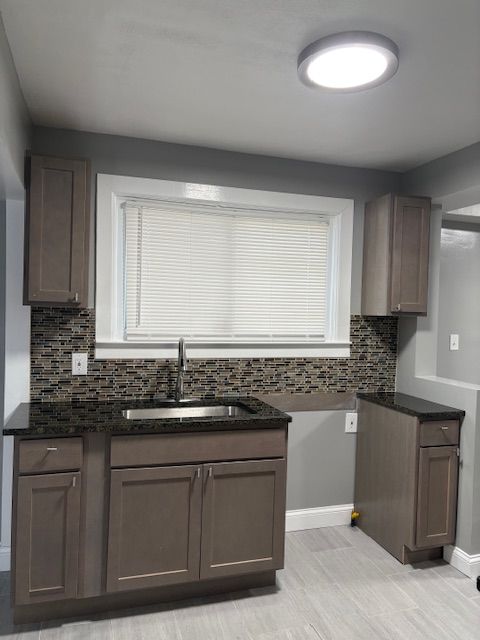 kitchen featuring sink, dark stone counters, decorative backsplash, and dark brown cabinetry