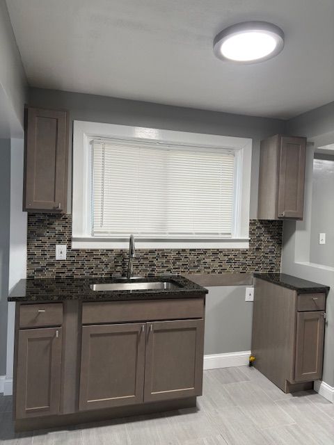 kitchen featuring dark stone countertops, backsplash, dark brown cabinets, and sink