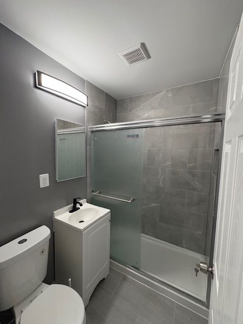 bathroom with toilet, a shower with door, and vanity