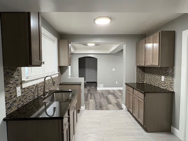 kitchen with sink, a tray ceiling, tasteful backsplash, and dark stone counters