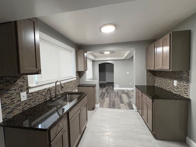 kitchen with sink, dark stone countertops, light hardwood / wood-style flooring, decorative backsplash, and a tray ceiling