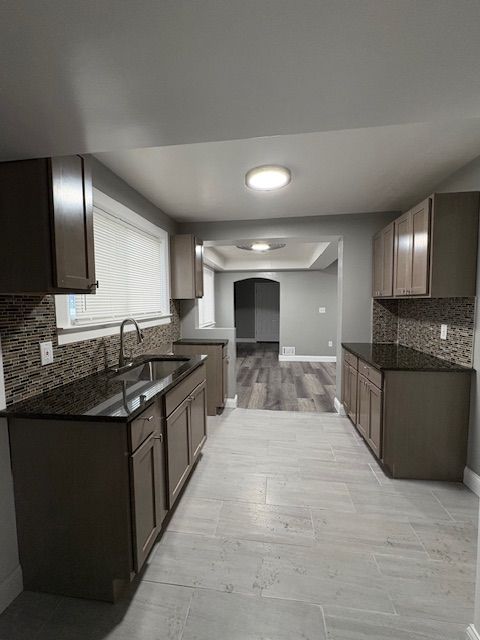 kitchen featuring sink, dark stone countertops, decorative backsplash, and dark brown cabinetry