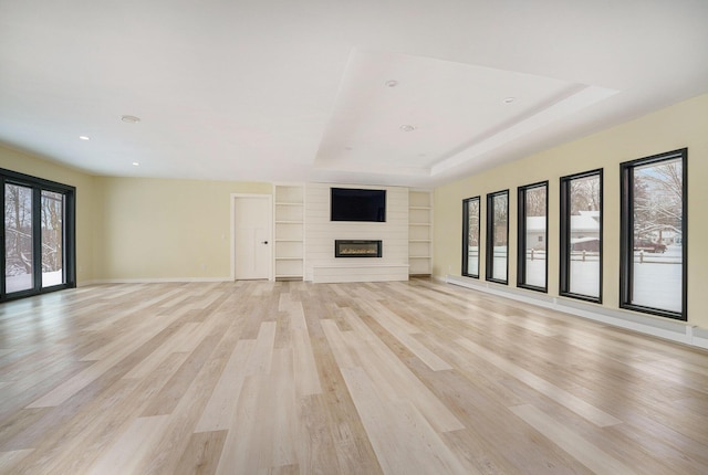 unfurnished living room with a fireplace, light wood-type flooring, a tray ceiling, and built in features