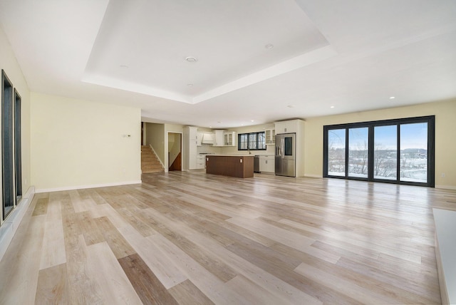 unfurnished living room featuring a raised ceiling and light wood-type flooring