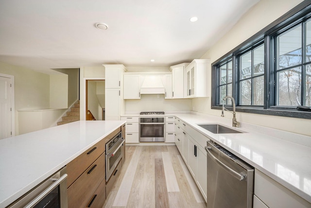 kitchen featuring light hardwood / wood-style floors, stainless steel appliances, custom range hood, sink, and white cabinetry