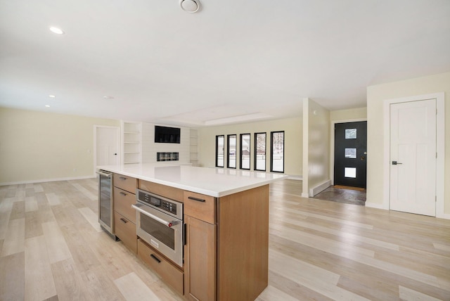 kitchen featuring beverage cooler, light wood-type flooring, a center island, a fireplace, and oven