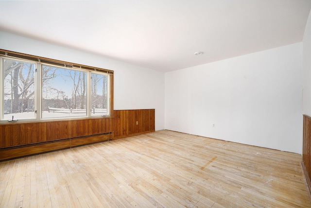 unfurnished room featuring baseboard heating, light hardwood / wood-style floors, and wooden walls