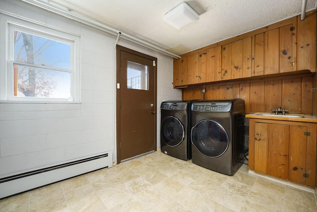 clothes washing area with sink, a textured ceiling, cabinets, a baseboard heating unit, and washer and dryer