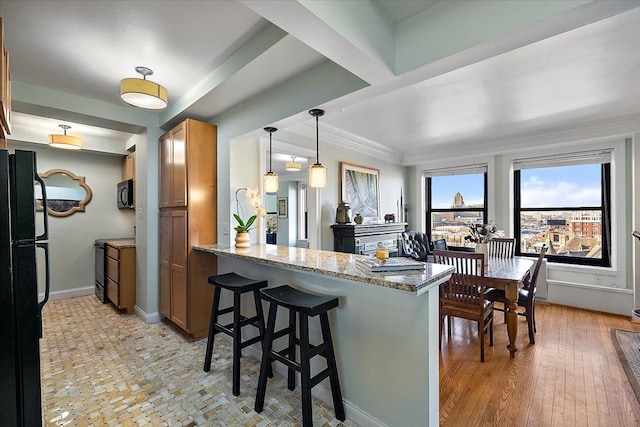 kitchen with kitchen peninsula, decorative light fixtures, light stone countertops, a breakfast bar, and black appliances