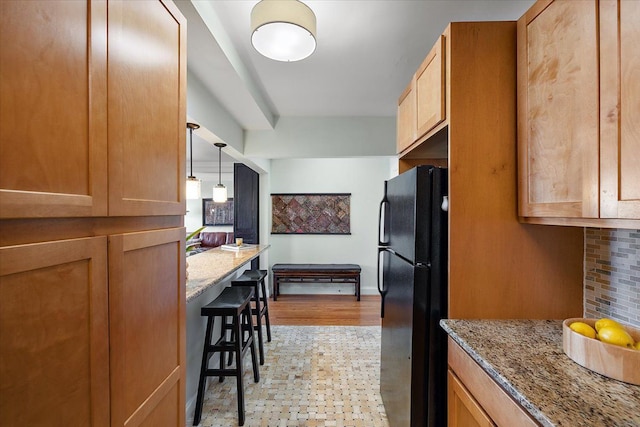 kitchen with light hardwood / wood-style floors, black refrigerator, decorative backsplash, pendant lighting, and light stone counters