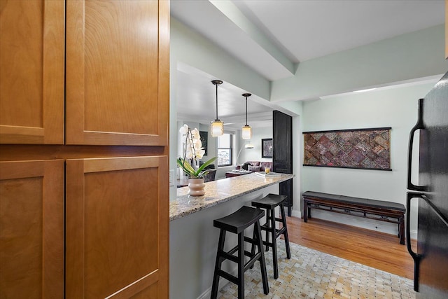 kitchen featuring light wood-type flooring, a breakfast bar area, light stone counters, and black refrigerator