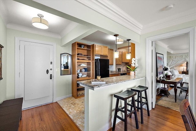 kitchen featuring kitchen peninsula, black fridge, a kitchen breakfast bar, dark hardwood / wood-style flooring, and pendant lighting