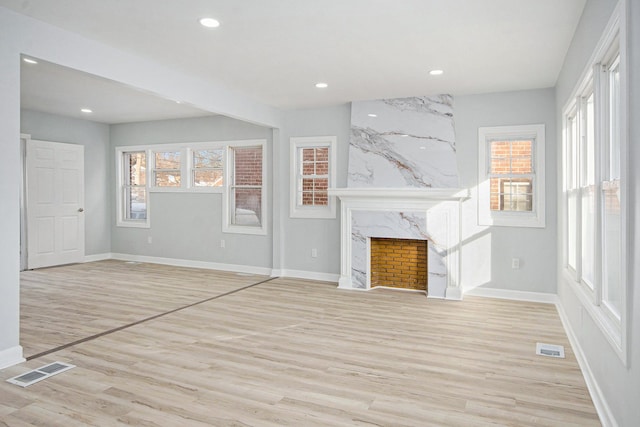 unfurnished living room featuring light wood-type flooring, a wealth of natural light, and a fireplace