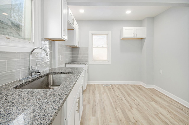 kitchen with decorative backsplash, sink, light stone counters, and white cabinetry