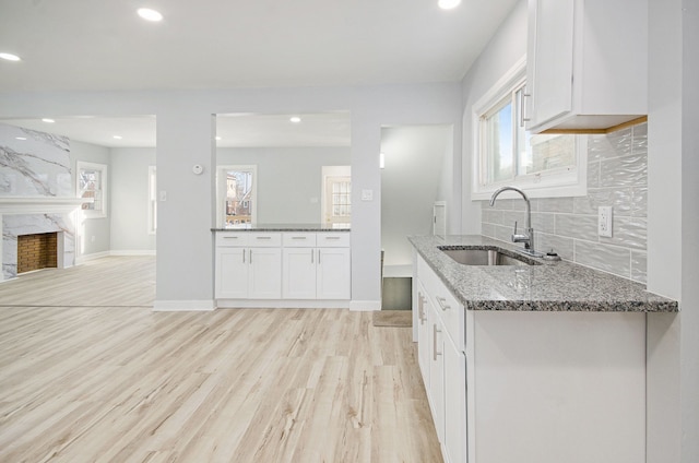 kitchen with white cabinets, a fireplace, tasteful backsplash, sink, and stone countertops