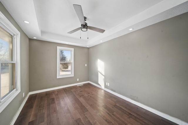 spare room with ceiling fan, a tray ceiling, and dark wood-type flooring