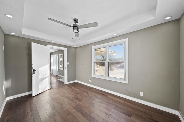 empty room featuring ceiling fan, dark hardwood / wood-style flooring, and a raised ceiling