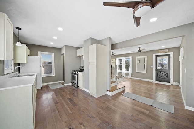 kitchen with stainless steel gas range, dark hardwood / wood-style flooring, sink, white cabinetry, and decorative light fixtures