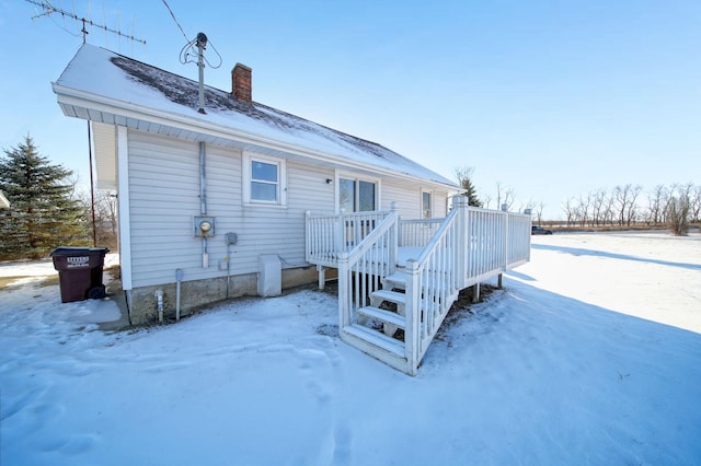 snow covered back of property with a wooden deck