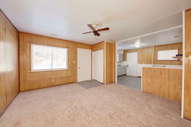 unfurnished living room with light colored carpet, wood walls, and ceiling fan