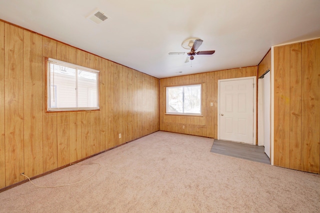 carpeted empty room with ceiling fan and wooden walls