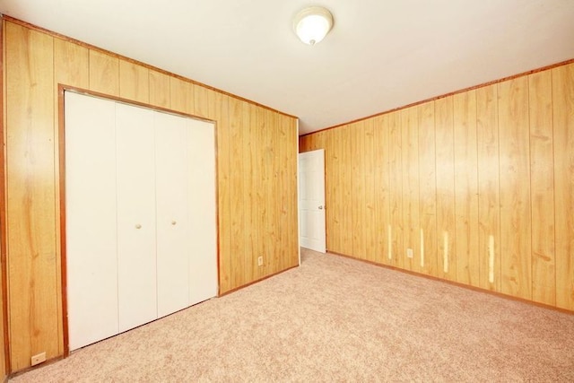 unfurnished bedroom featuring a closet, light carpet, and wooden walls