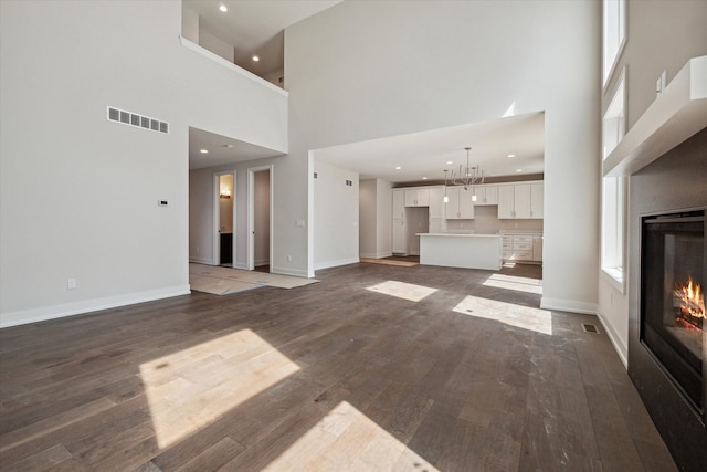 unfurnished living room featuring a wealth of natural light, dark hardwood / wood-style flooring, a towering ceiling, and a chandelier