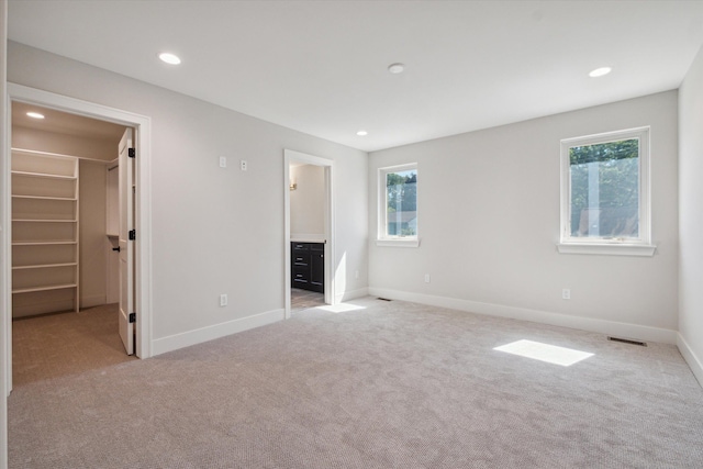 unfurnished bedroom with light colored carpet, ensuite bath, multiple windows, and a spacious closet