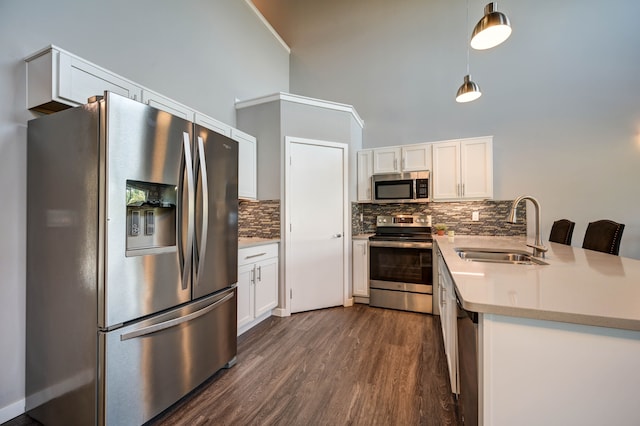 kitchen with dark wood-type flooring, appliances with stainless steel finishes, a peninsula, white cabinets, and a sink