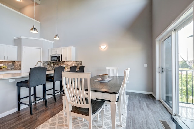 dining space with visible vents, baseboards, wood finished floors, and a towering ceiling