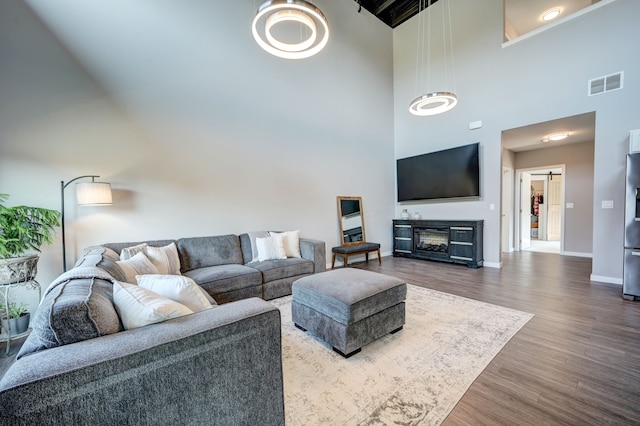 living area with visible vents, a towering ceiling, baseboards, and wood finished floors