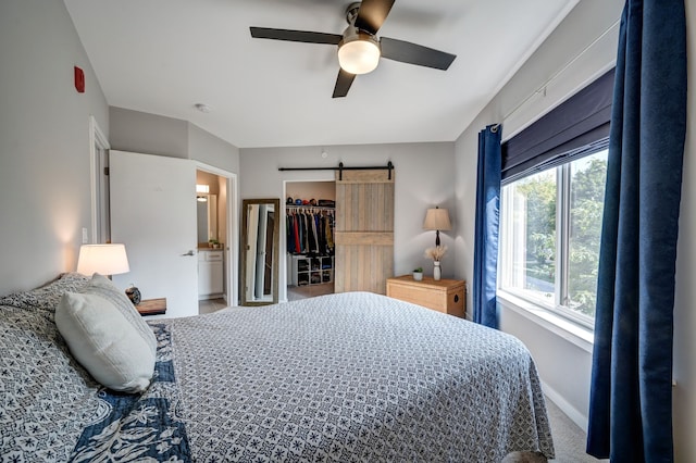 bedroom with a ceiling fan, a barn door, carpet, baseboards, and a spacious closet