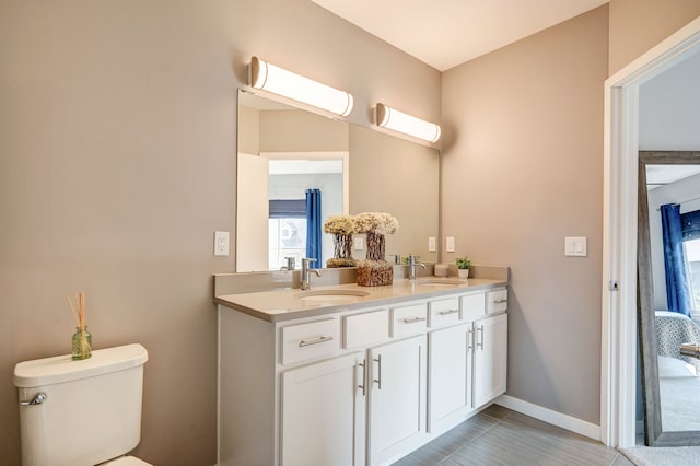 bathroom featuring double vanity, toilet, baseboards, and a sink