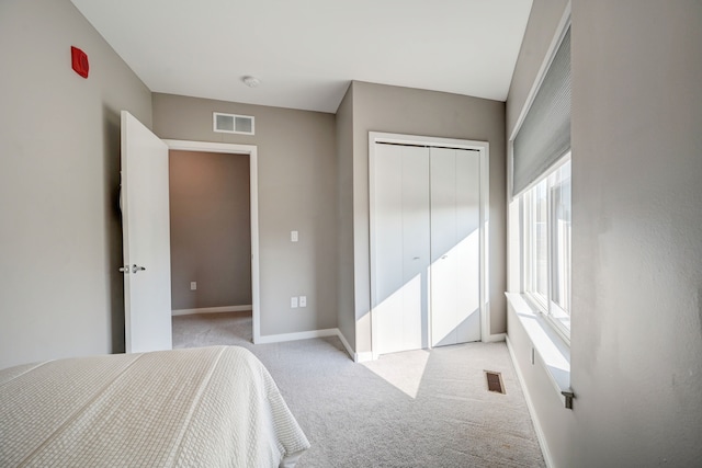 bedroom with a closet, visible vents, light colored carpet, and baseboards