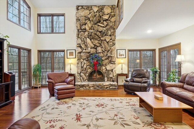 living room featuring a towering ceiling, french doors, hardwood / wood-style floors, a wealth of natural light, and a stone fireplace