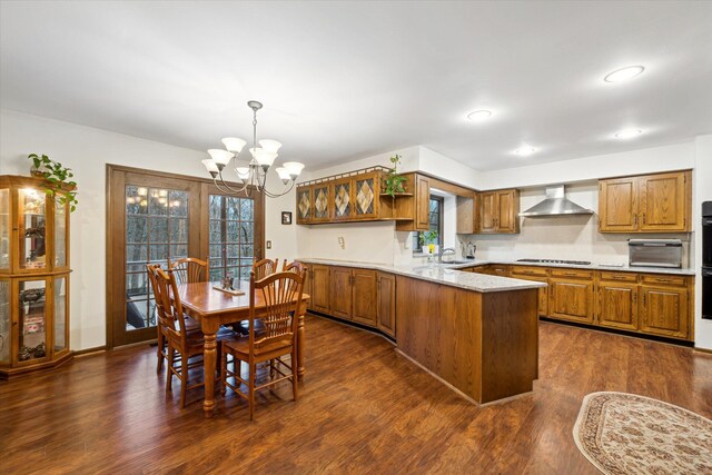 kitchen featuring an inviting chandelier, black gas cooktop, wall chimney exhaust hood, kitchen peninsula, and dark hardwood / wood-style flooring